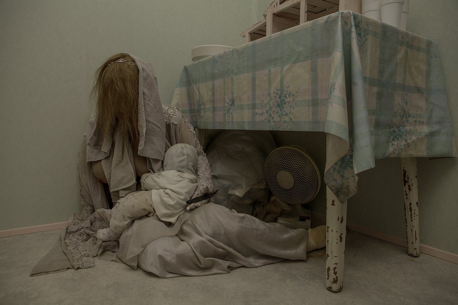 SIGNA, a veiled figure and a doll under a table