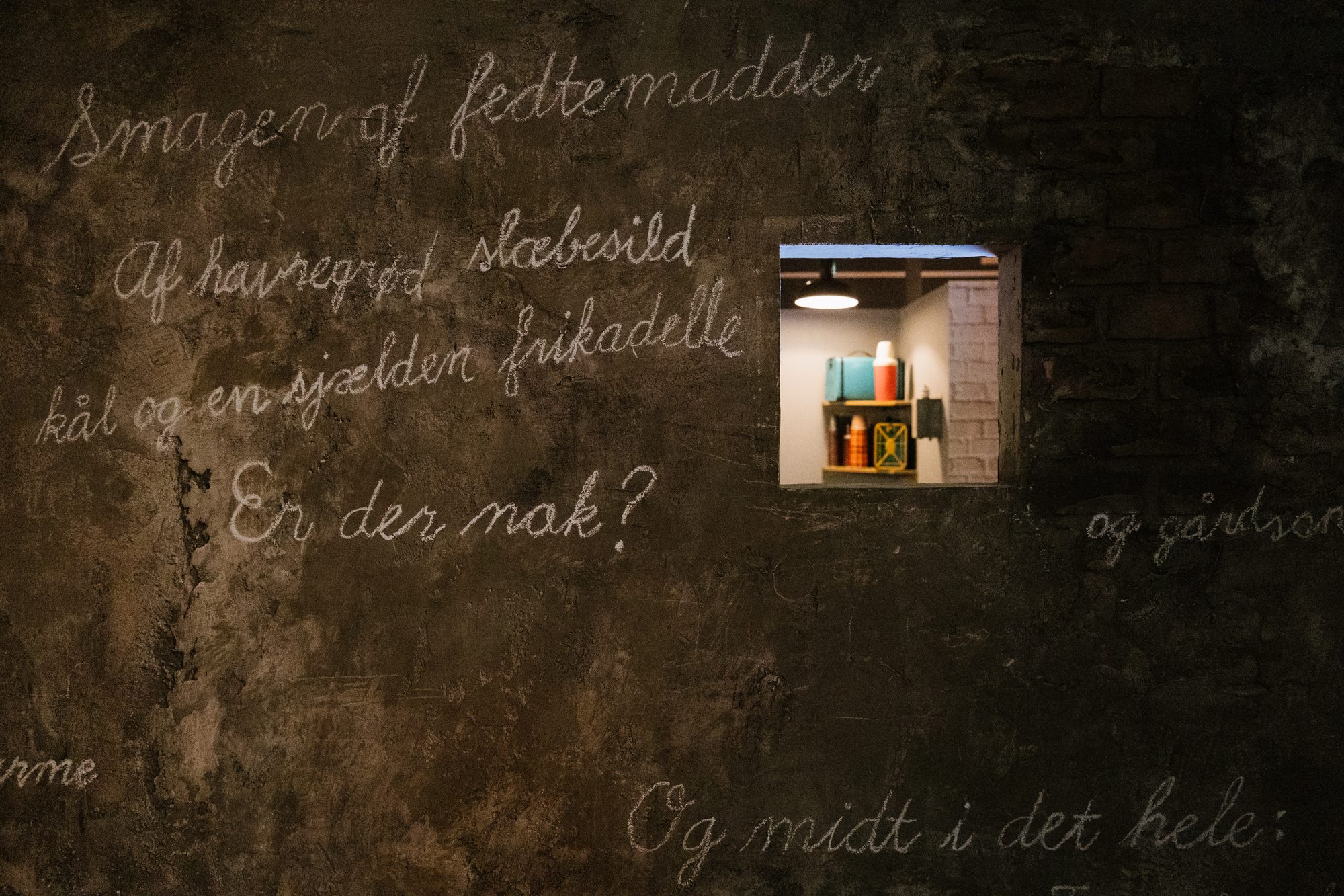 Kvindeliv, chalk handwriting on a dark wall with a small lit window