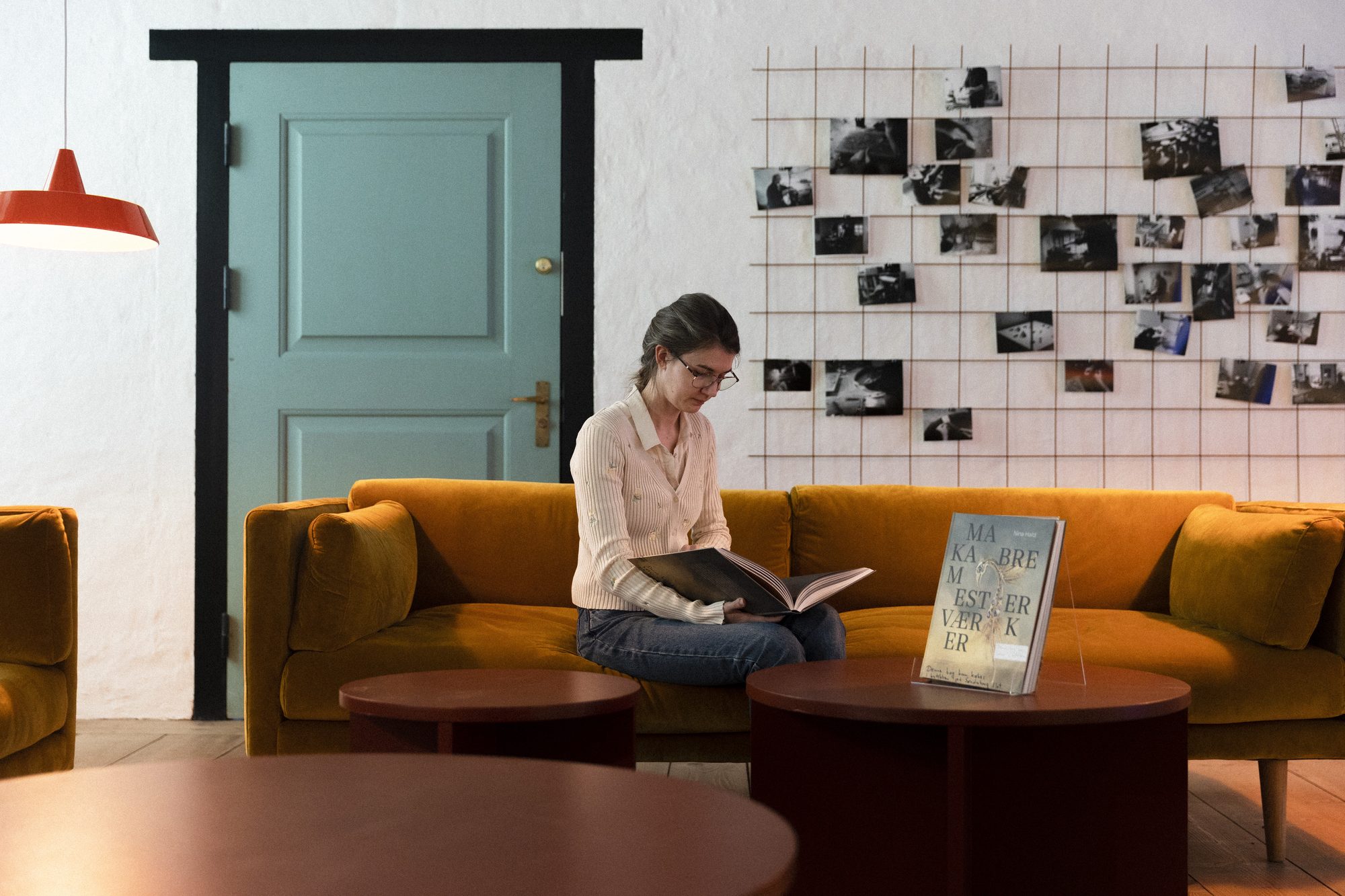 Makabre Mesterværker, reading room with yellow velvet sofa and a wall of photographs
