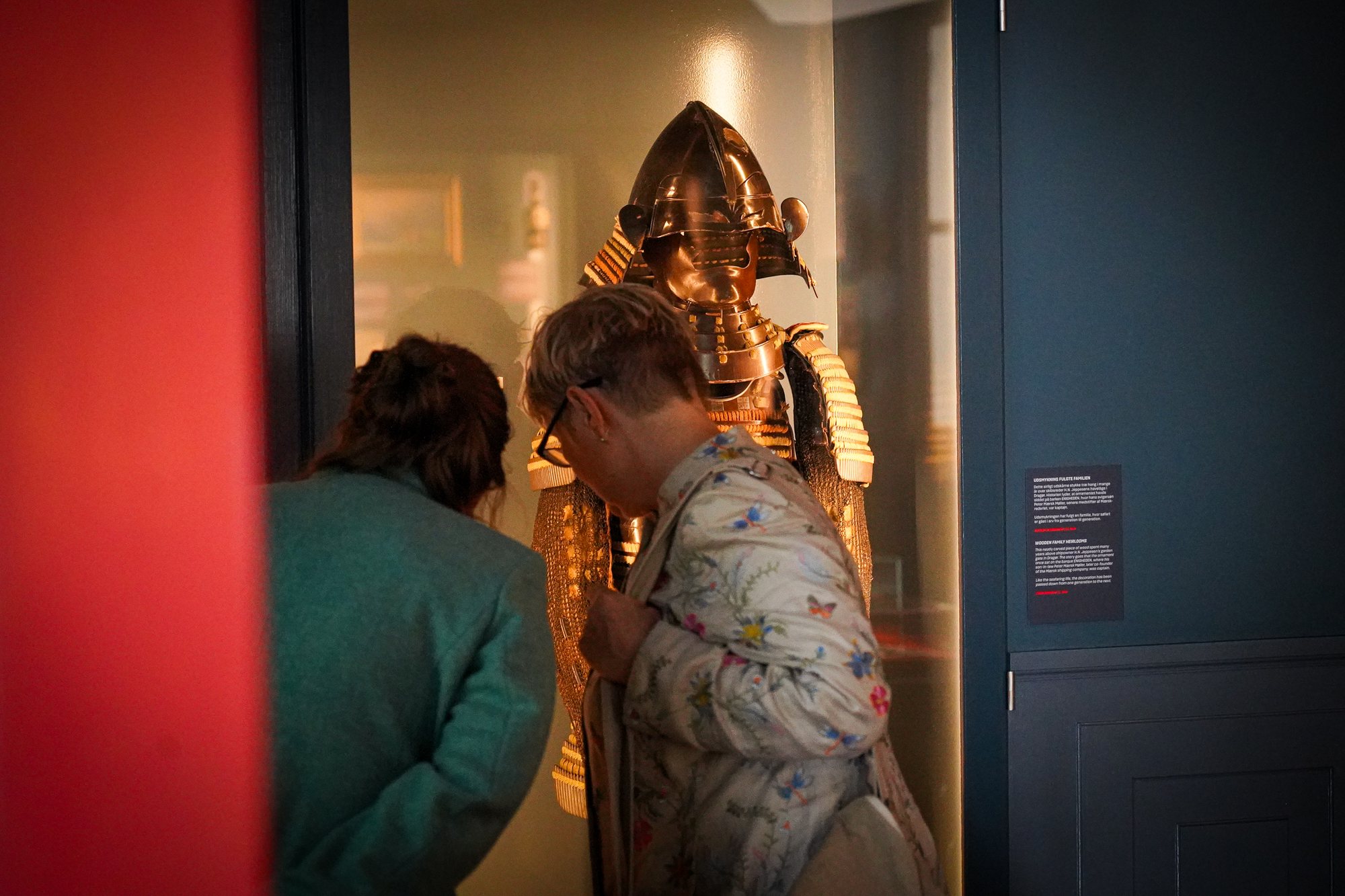 Søfarer, two visitors leaning in to the Japanese armour in its vitrine
