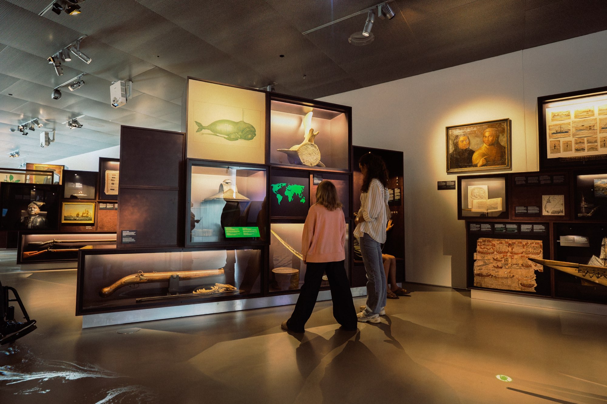 Søfarer, two visitors at the stacked vitrines with the whale drawing, the vertebra and the flintlock
