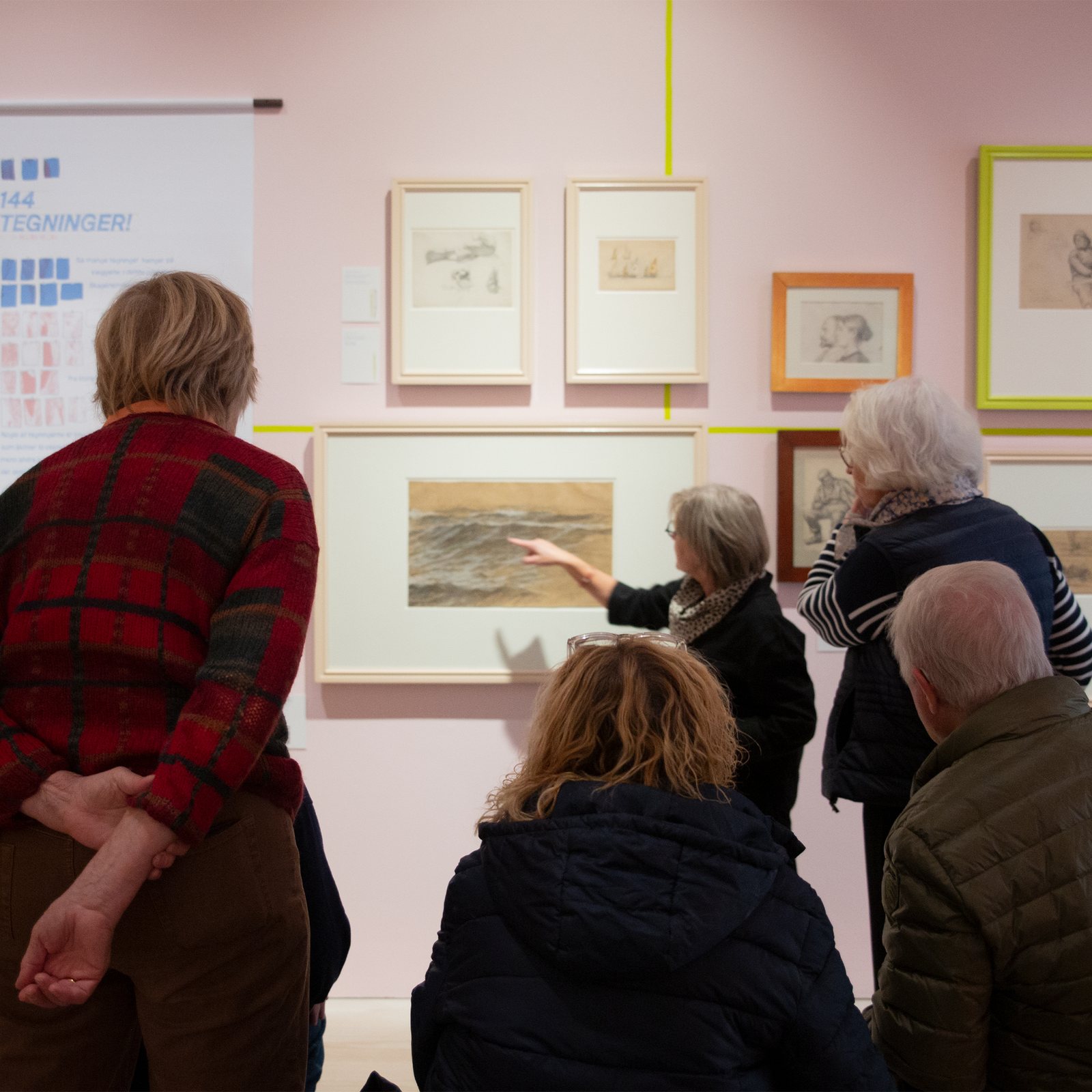 Tegn Amok, a group of visitors at the wall of drawings with a guide